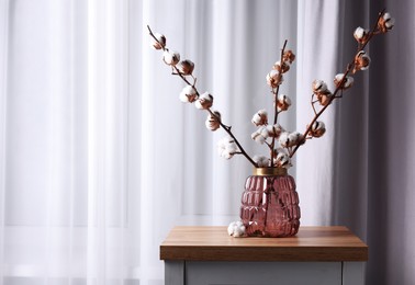 Photo of Cotton branches with fluffy flowers in vase on wooden table indoors. Space for text