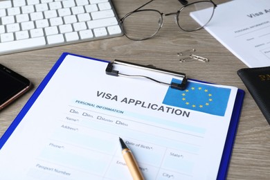 Photo of Visa application form for immigration to European Union, pen and glasses on wooden table, closeup