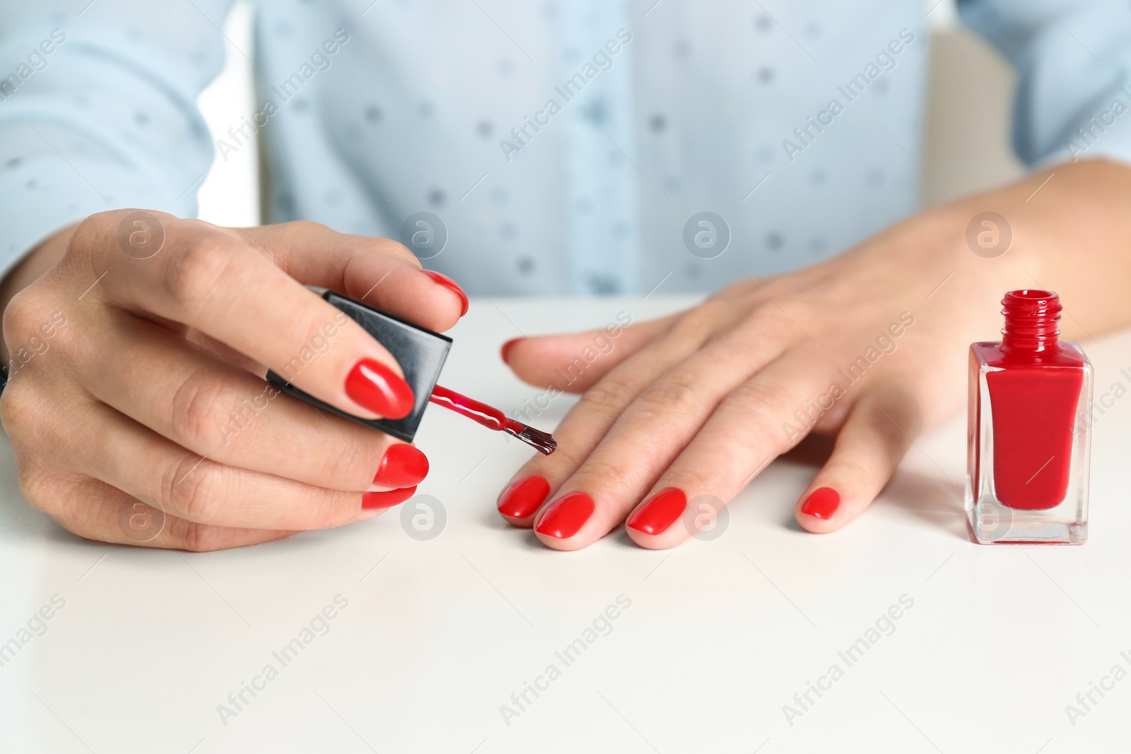 Photo of Woman applying bright nail polish at white table, closeup