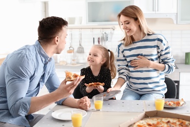 Pregnant woman and her family eating pizza in kitchen