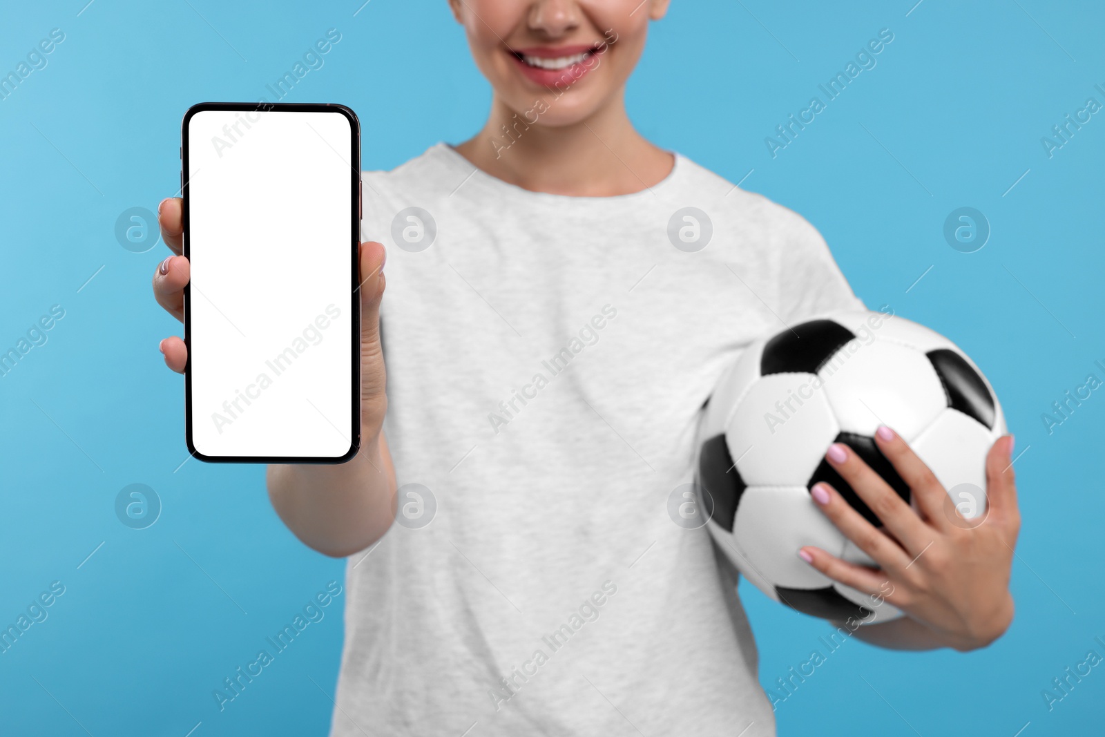 Photo of Happy sports fan with soccer ball and smartphone on light blue background, closeup