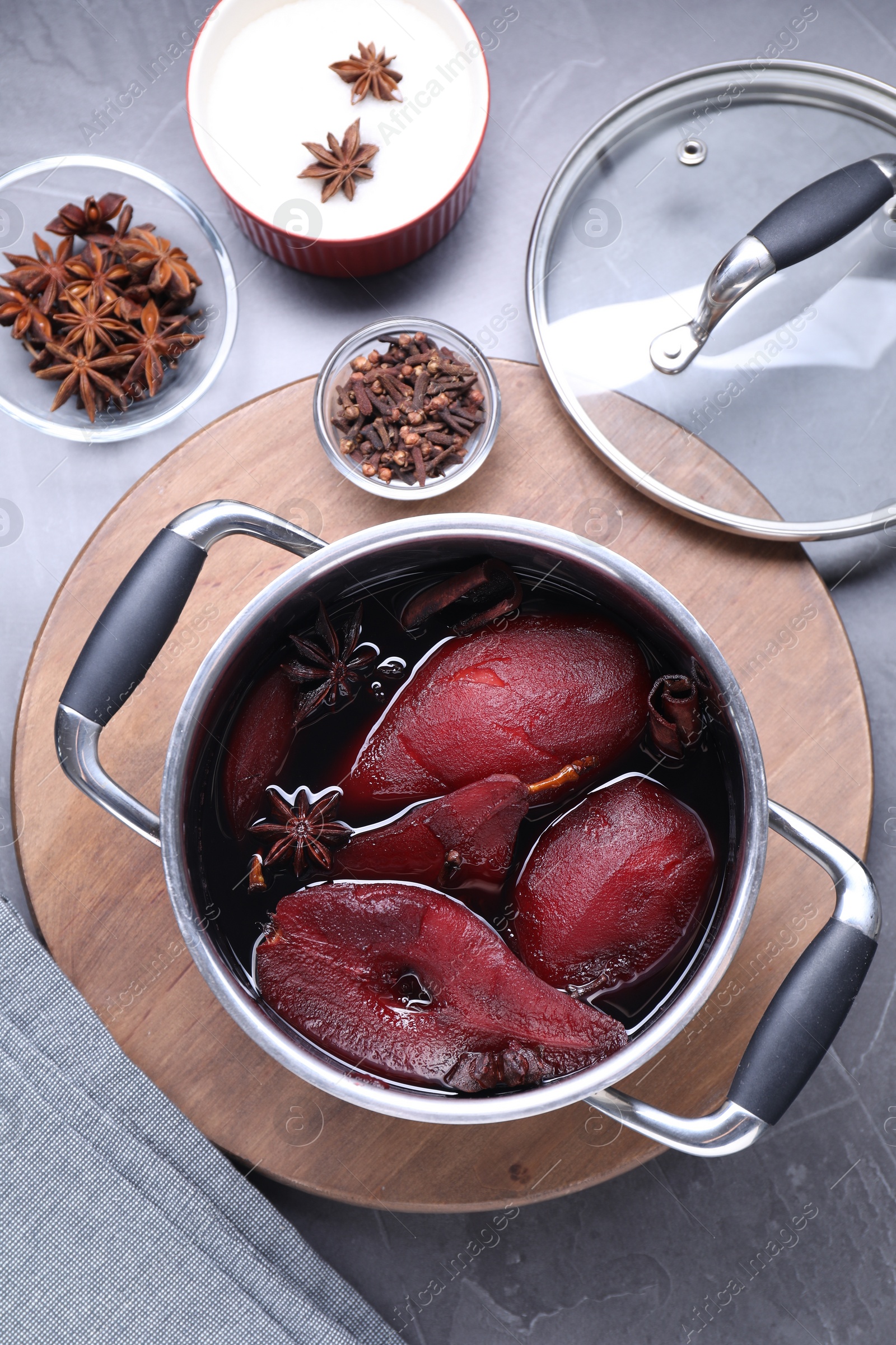 Photo of Tasty red wine poached pears and spices in pot on grey table, flat lay