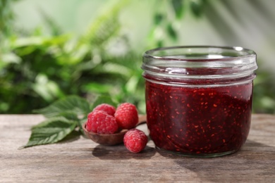 Delicious jam in glass jar and fresh raspberries on wooden table
