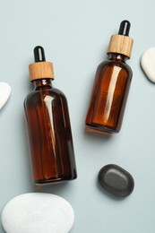 Flat lay composition with bottles of face serum and spa stones on light grey background