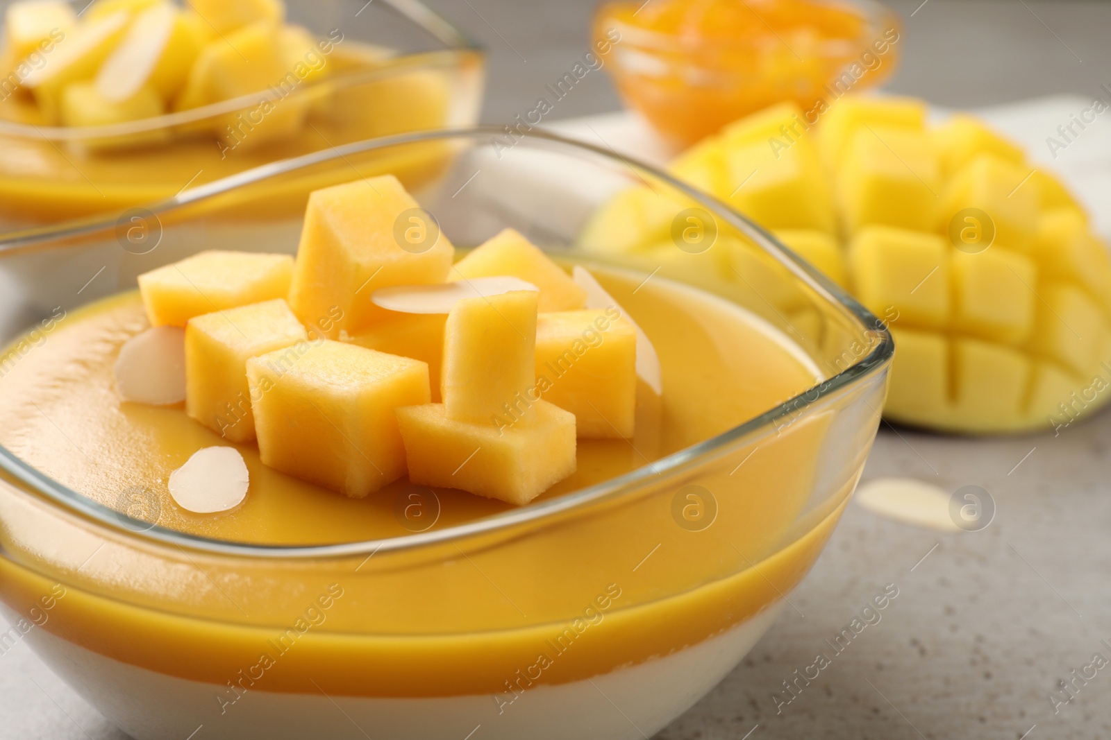 Photo of Delicious panna cotta with mango coulis and fresh fruit pieces on grey table, closeup