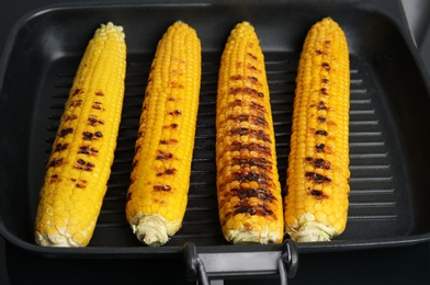 Photo of Grill pan with tasty fresh corn cobs on stove, closeup