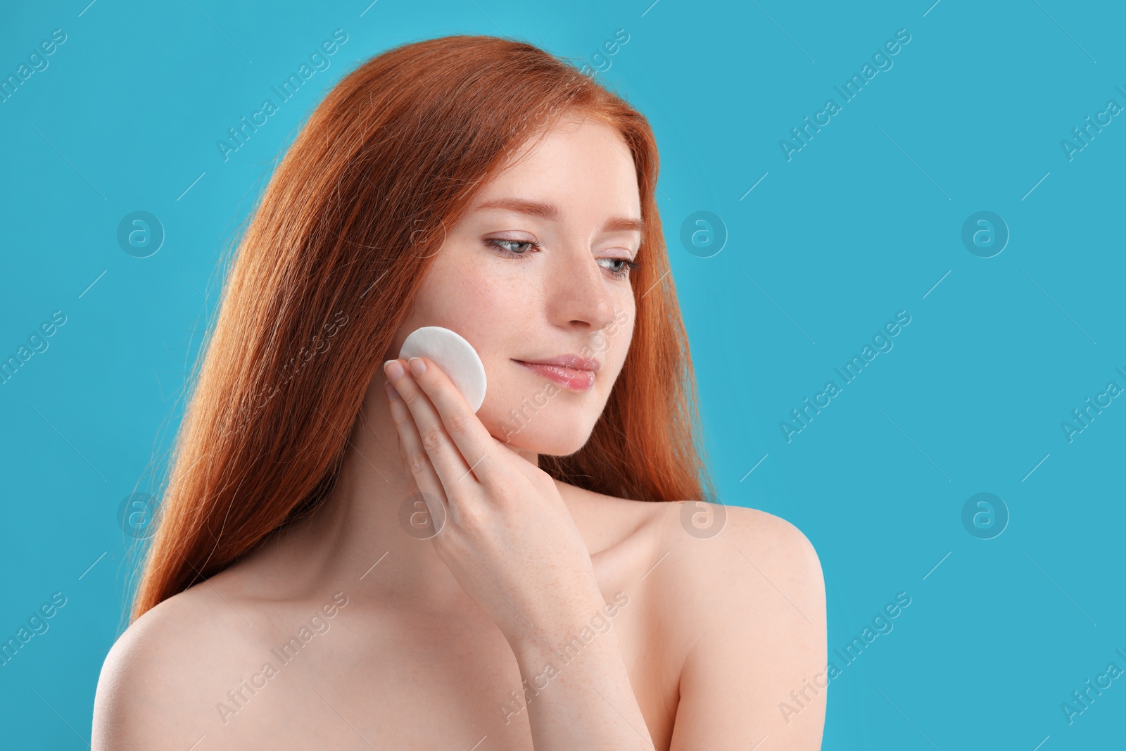 Photo of Beautiful woman with freckles wiping face on light blue background. Space for text