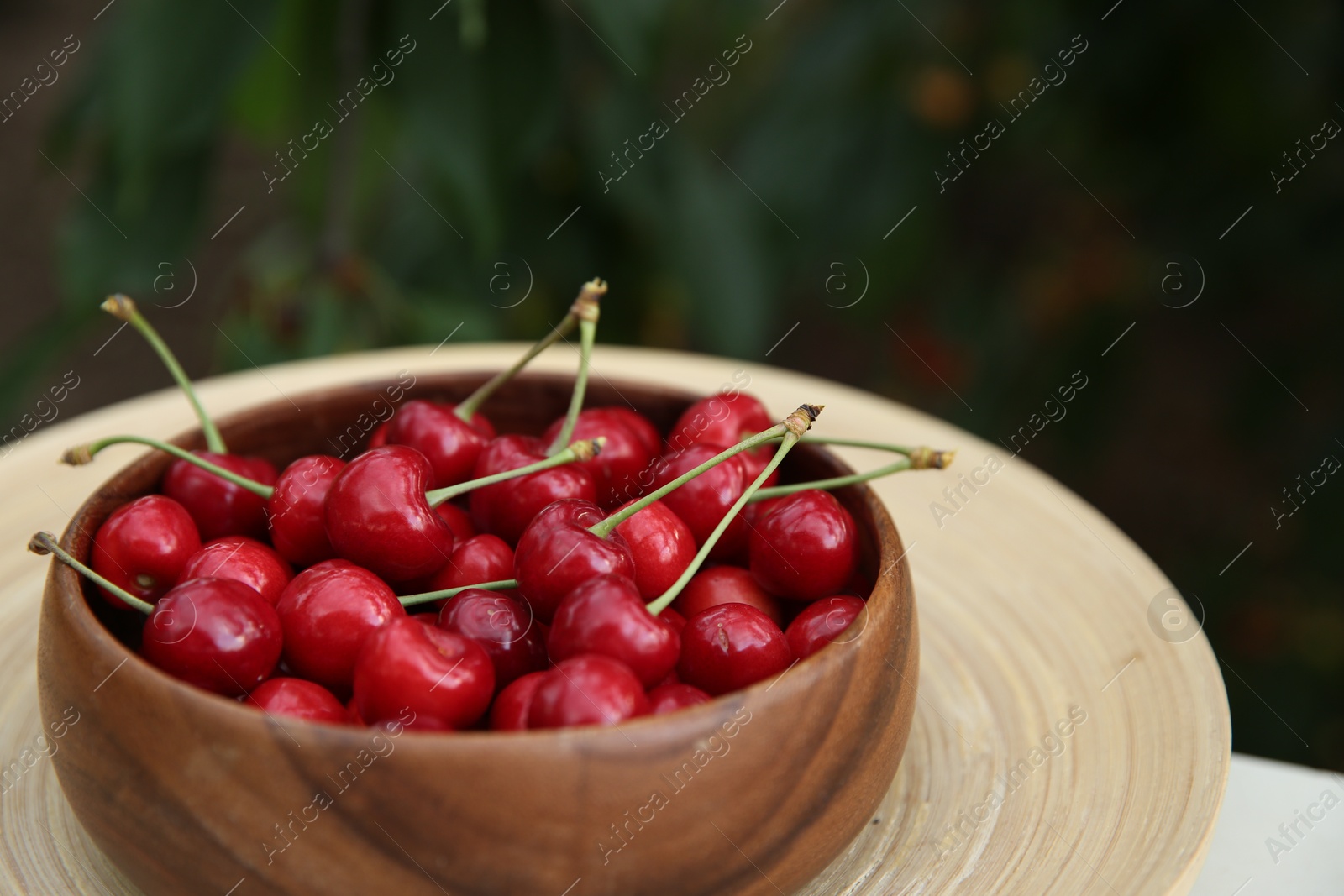 Photo of Tasty ripe red cherries in wooden bowl outdoors