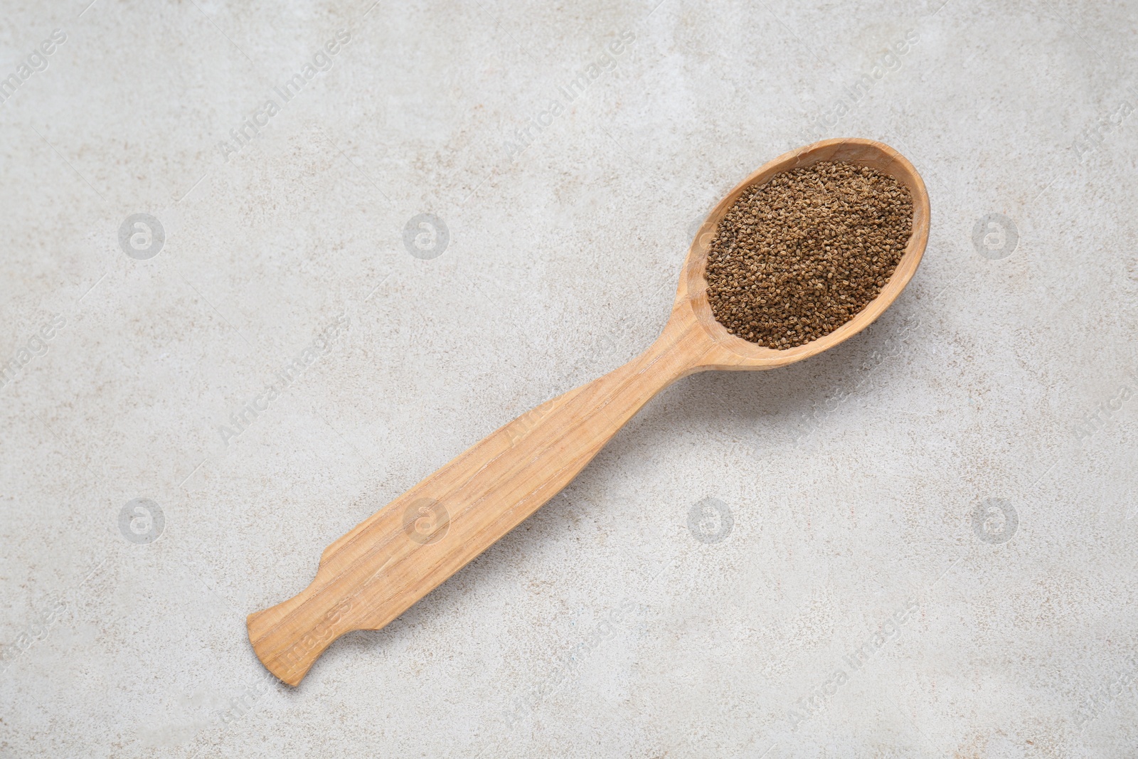 Photo of Spoon of celery seeds on light grey textured table, top view