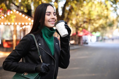 Photo of Beautiful young woman with cup of coffee on city street. Autumn walk