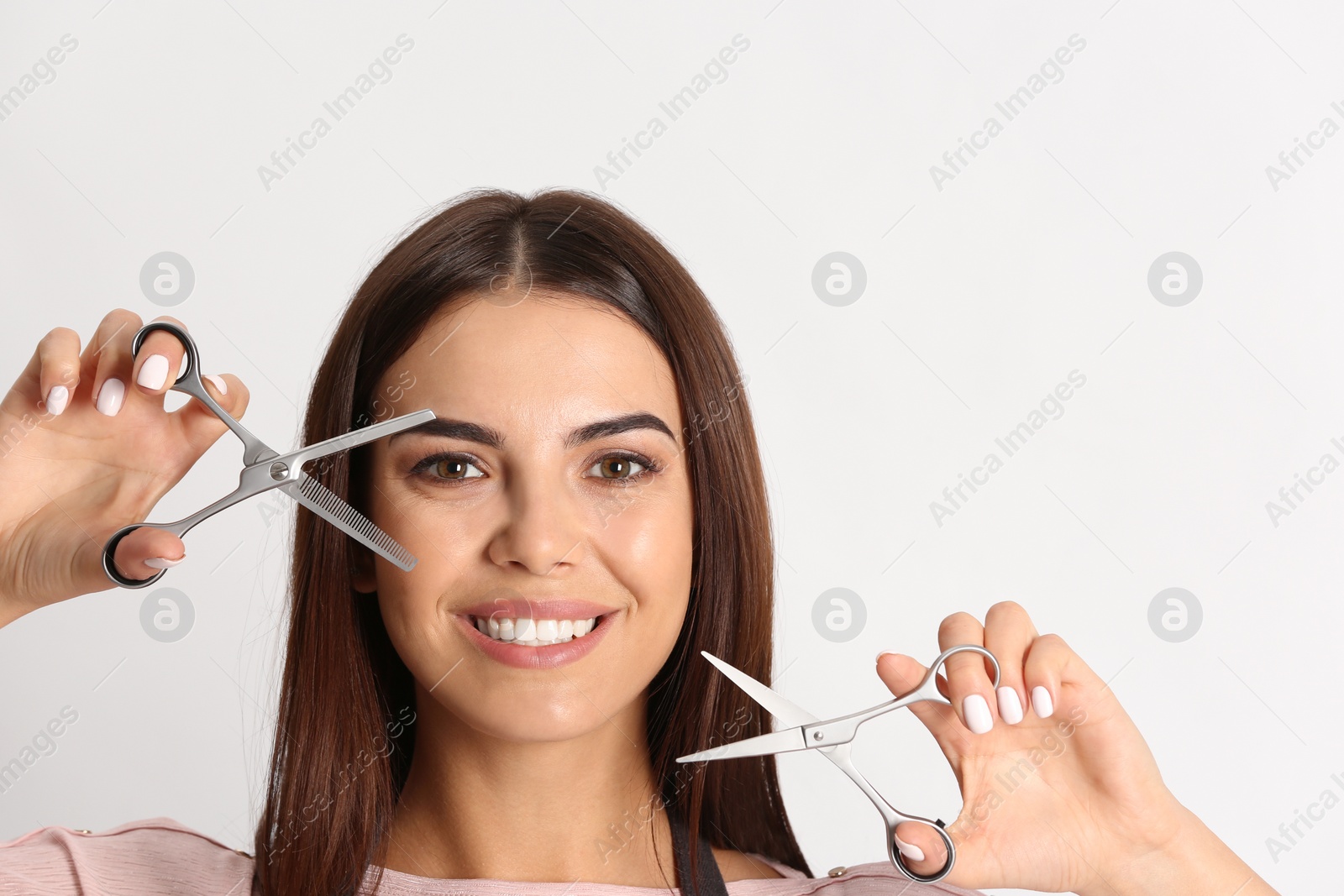 Photo of Young hairstylist holding professional scissors on light background