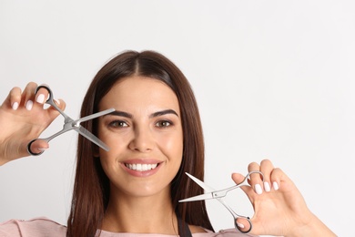 Photo of Young hairstylist holding professional scissors on light background