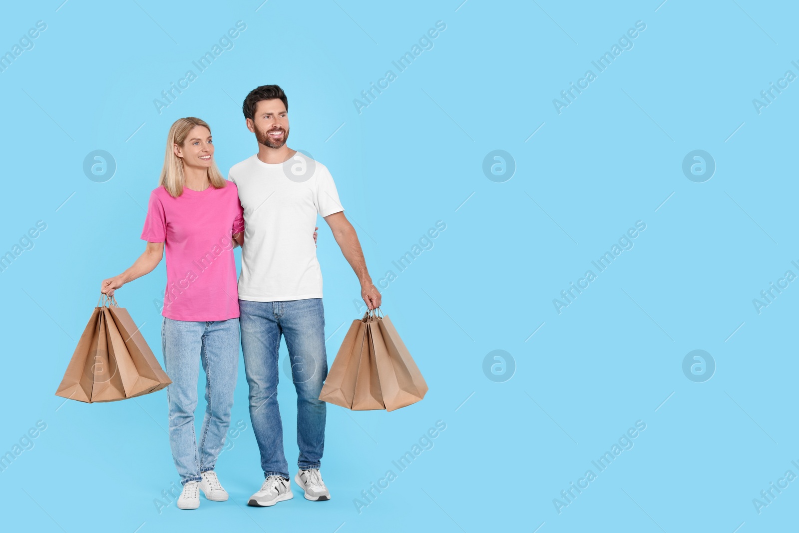 Photo of Family shopping. Happy couple with many paper bags on light blue background. Space for text