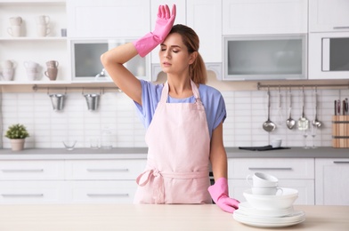 Photo of Tired woman near table with clean dishes and cups in kitchen