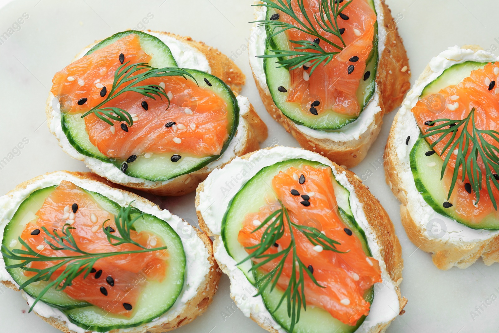 Photo of Tasty canapes with salmon, cucumber and cream cheese on board, top view