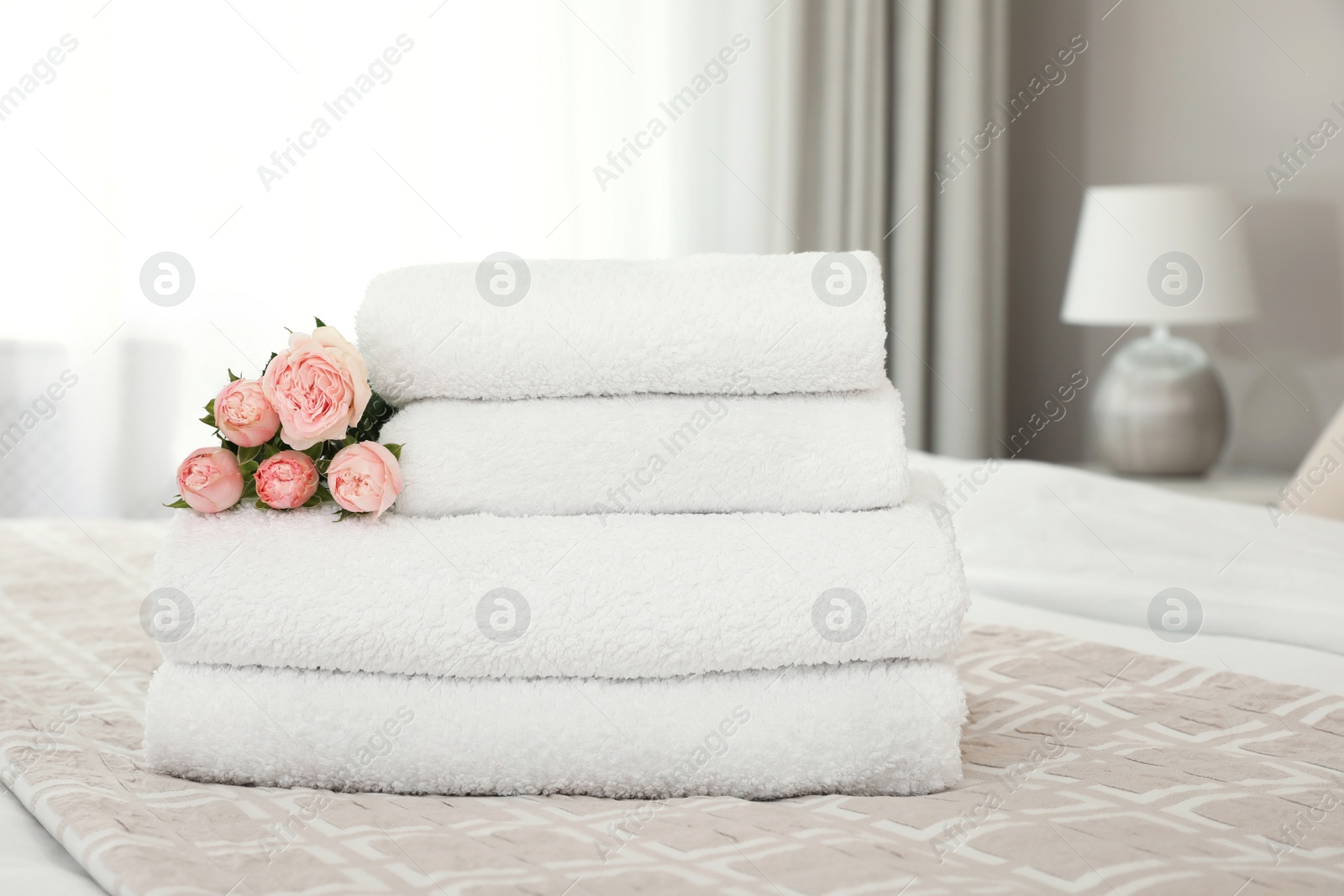 Photo of Stack of fresh towels with flowers on bed indoors