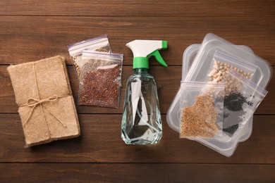 Microgreens growing kit. Different seeds, mats, containers and spray bottle on wooden table, flat lay