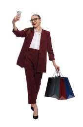 Stylish young businesswoman with shopping bags taking selfie on white background