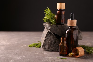 Photo of Essential oil in bottles, dropper and rosemary on grey table, space for text