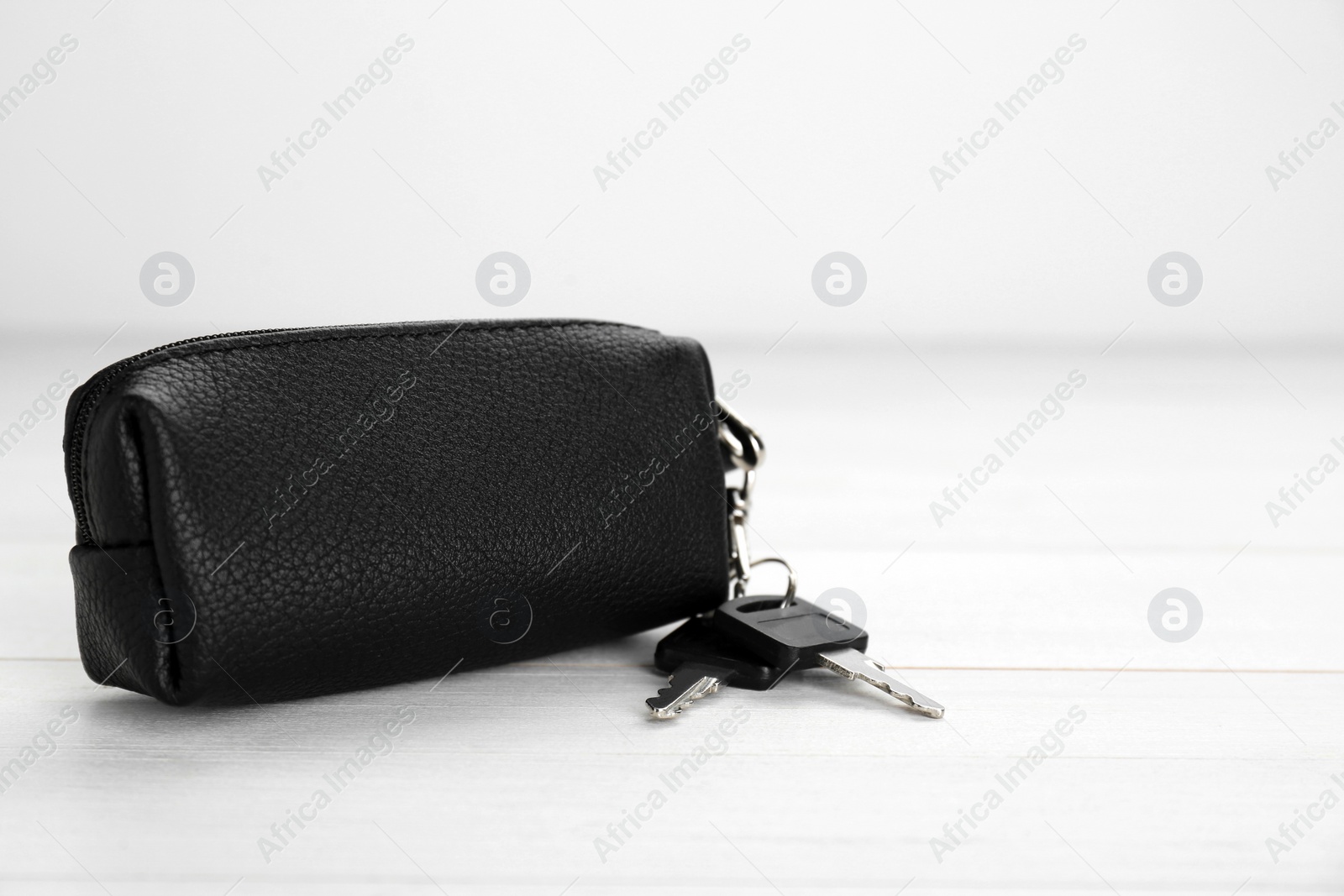 Photo of Leather case with keys on white wooden table, closeup. Space for text