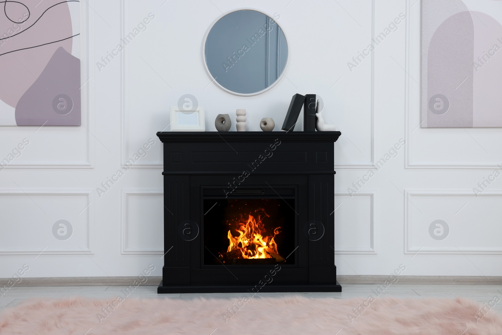 Photo of Black stylish fireplace with accessories under round mirror in cosy living room