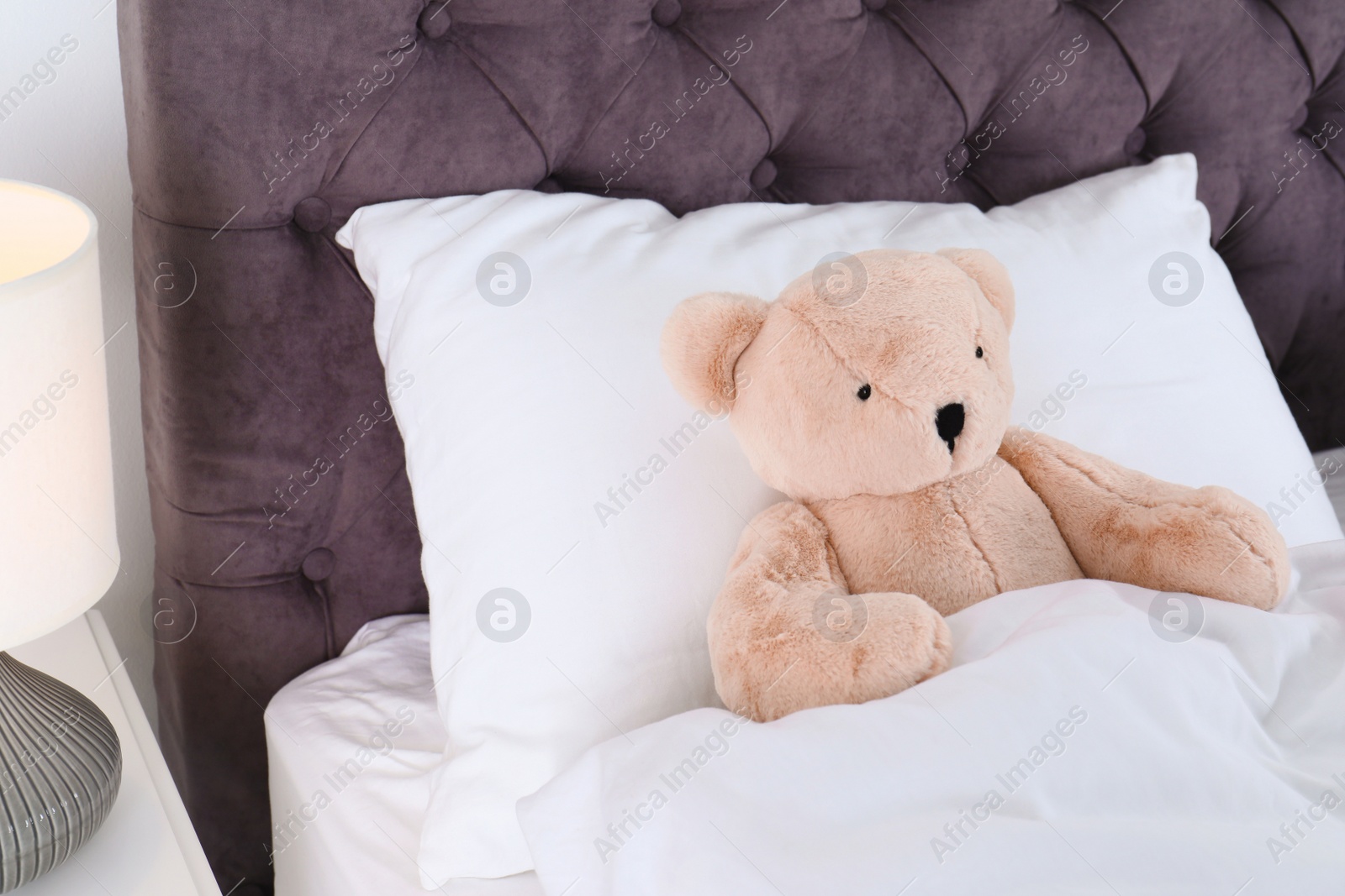 Photo of Cute teddy bear lying in bed indoors. Space for text