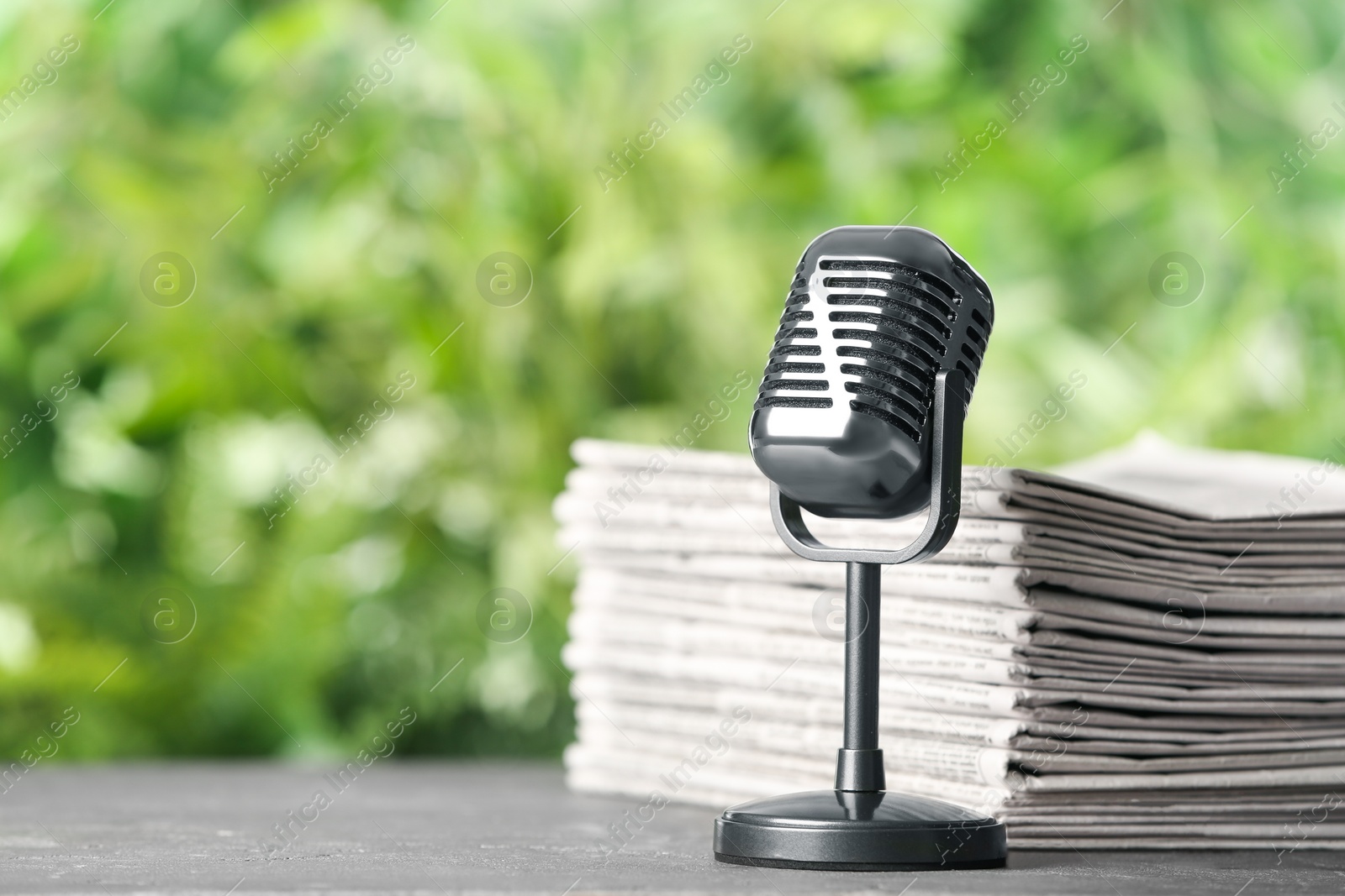 Photo of Newspapers and vintage microphone on grey table against blurred green background, space for text. Journalist's work