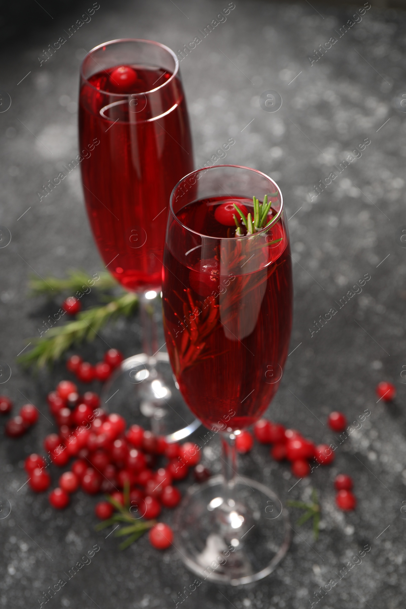 Photo of Tasty cranberry cocktail with rosemary in glasses on gray table, closeup