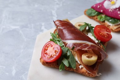 Photo of Delicious sandwich with cheese, prosciutto, tomato and arugula on light marble table, closeup