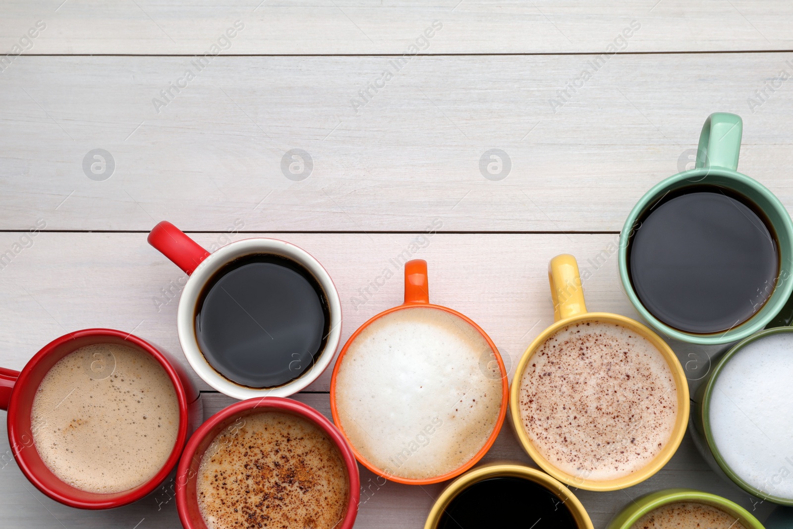 Photo of Many different cups with aromatic hot coffee on white wooden table, flat lay. Space for text