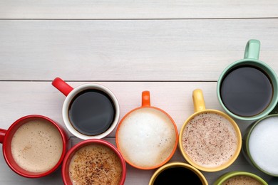 Many different cups with aromatic hot coffee on white wooden table, flat lay. Space for text