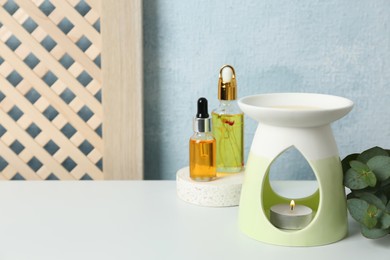 Photo of Aroma lamp and essential oils on white table. Space for text