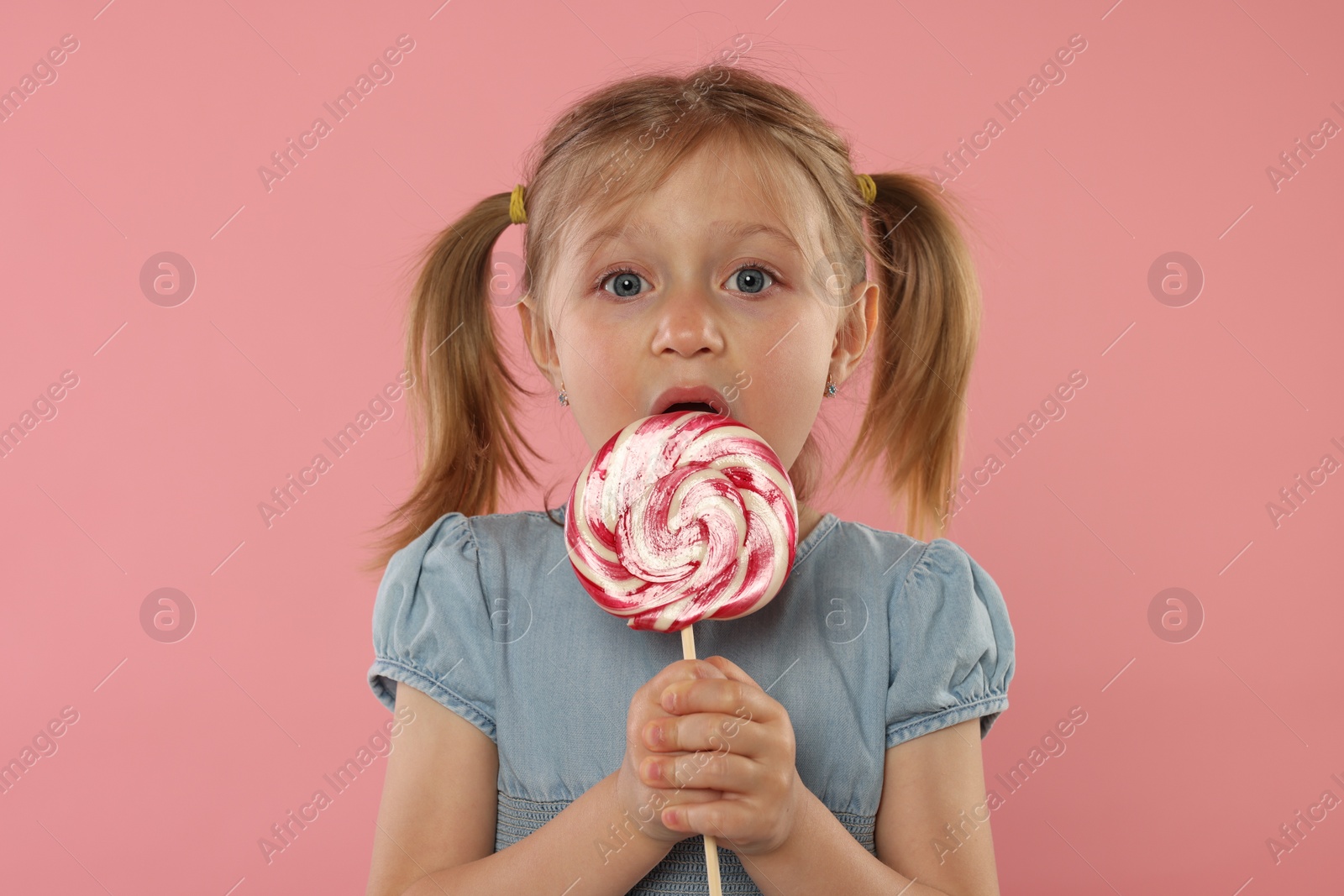 Photo of Portrait of cute girl licking lollipop on pink background