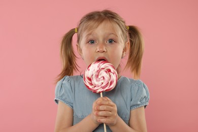 Photo of Portrait of cute girl licking lollipop on pink background