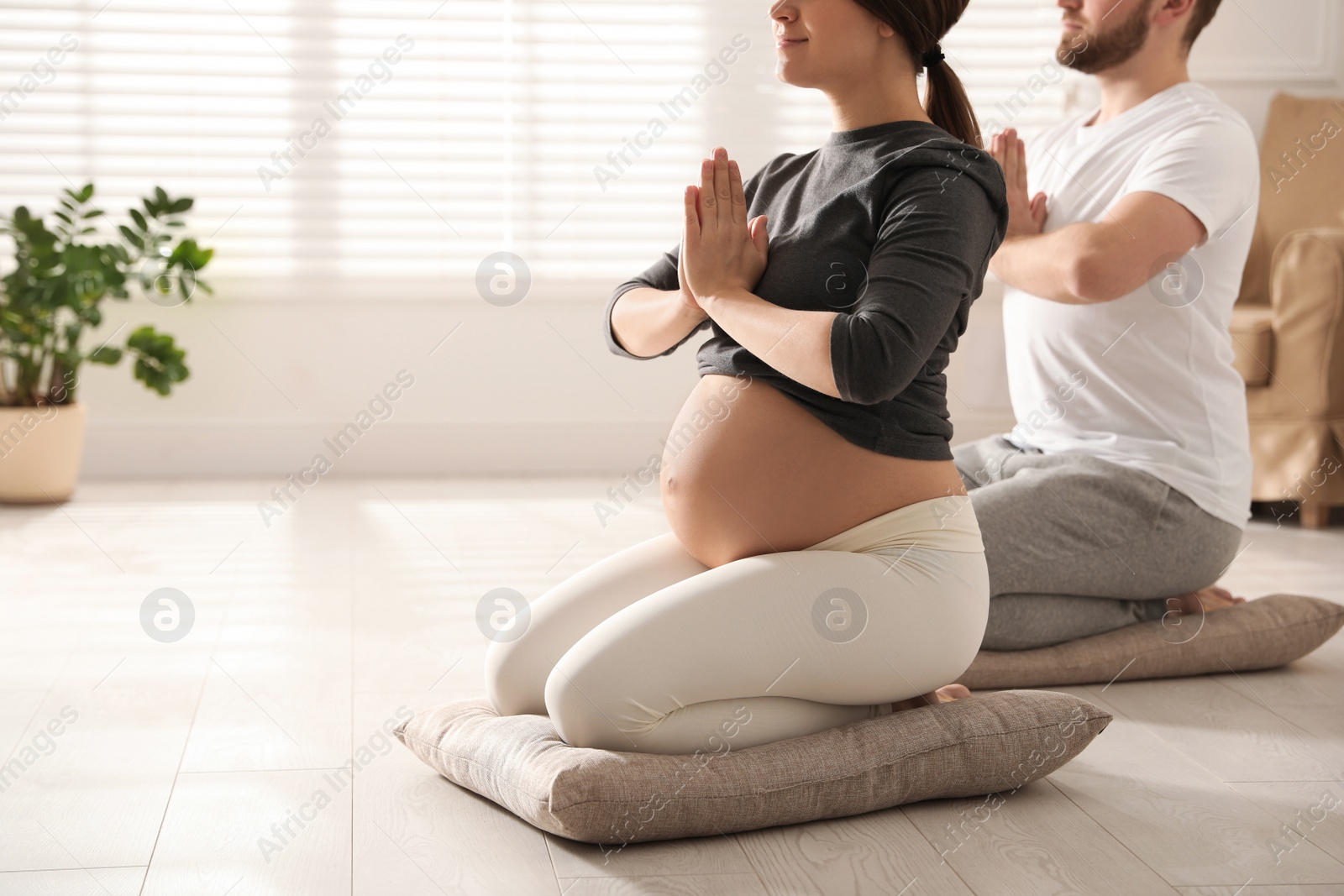Photo of Young pregnant woman with her husband practicing yoga at home, closeup. Space for text