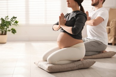 Young pregnant woman with her husband practicing yoga at home, closeup. Space for text