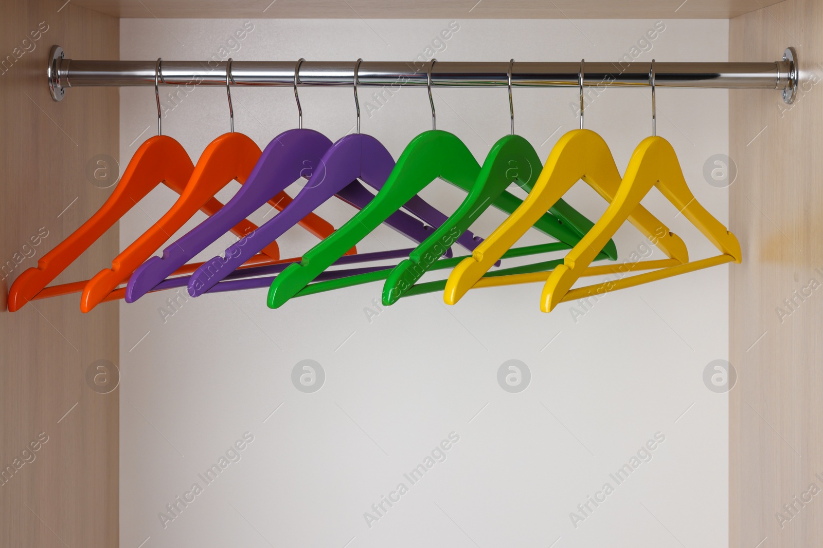 Photo of Set of bright clothes hangers on wardrobe rail