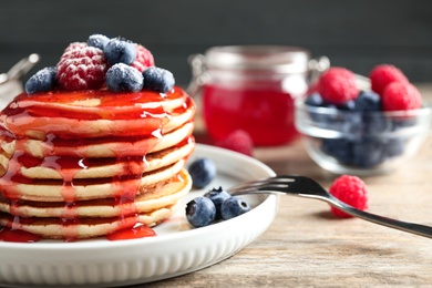 Delicious pancakes with fresh berries and syrup on wooden table, closeup