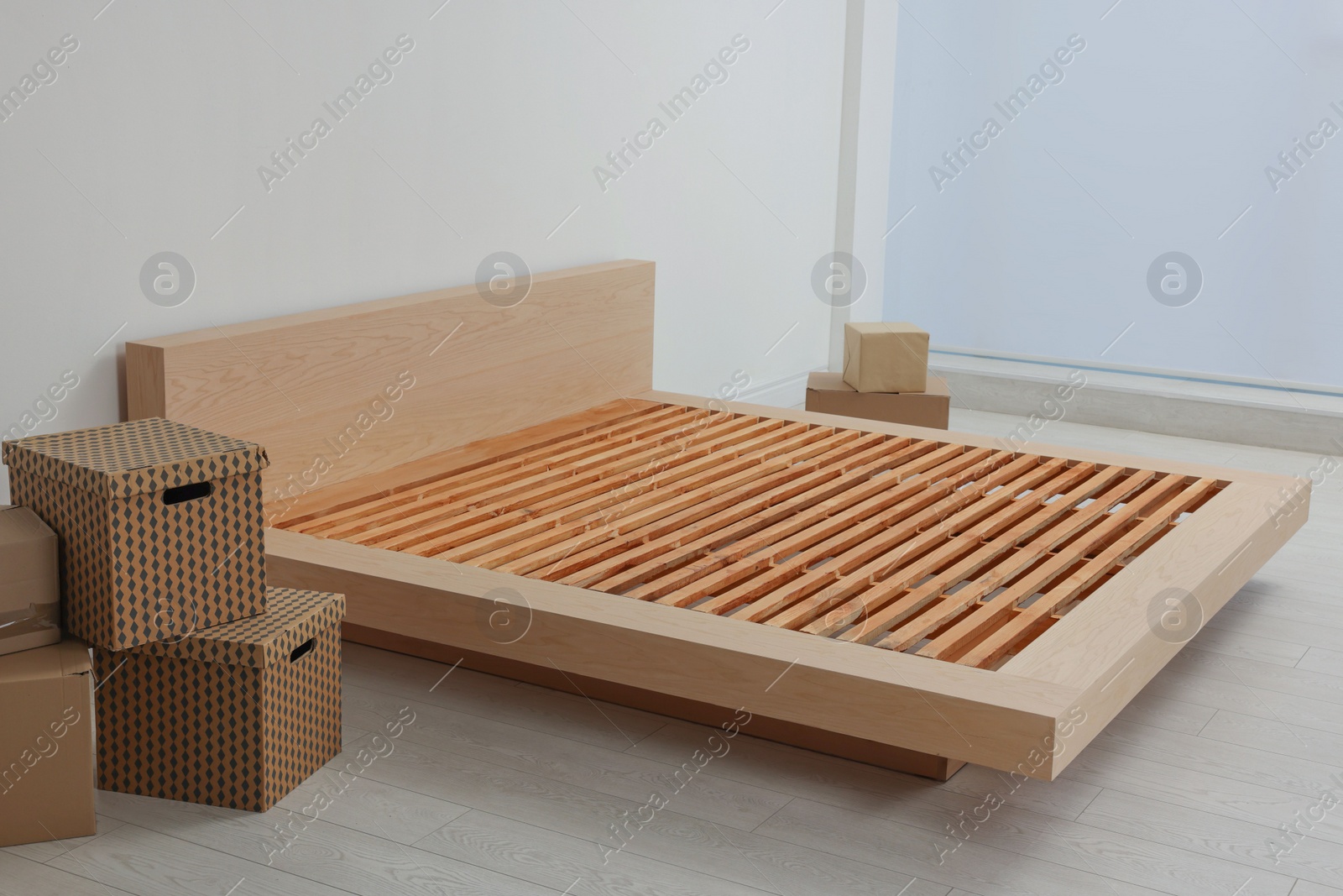 Photo of New wooden bed frame and moving boxes indoors