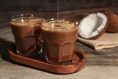 Pouring delicious syrup into glass with tasty coffee at wooden table, closeup