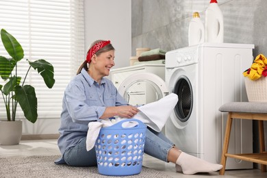 Photo of Happy housewife putting laundry into washing machine at home