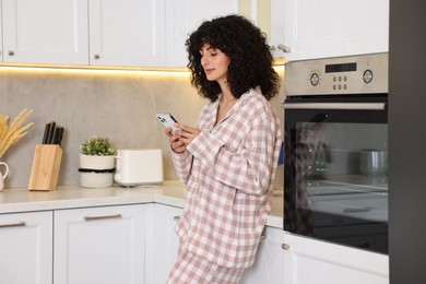 Photo of Beautiful young woman in stylish pyjama using smartphone in kitchen