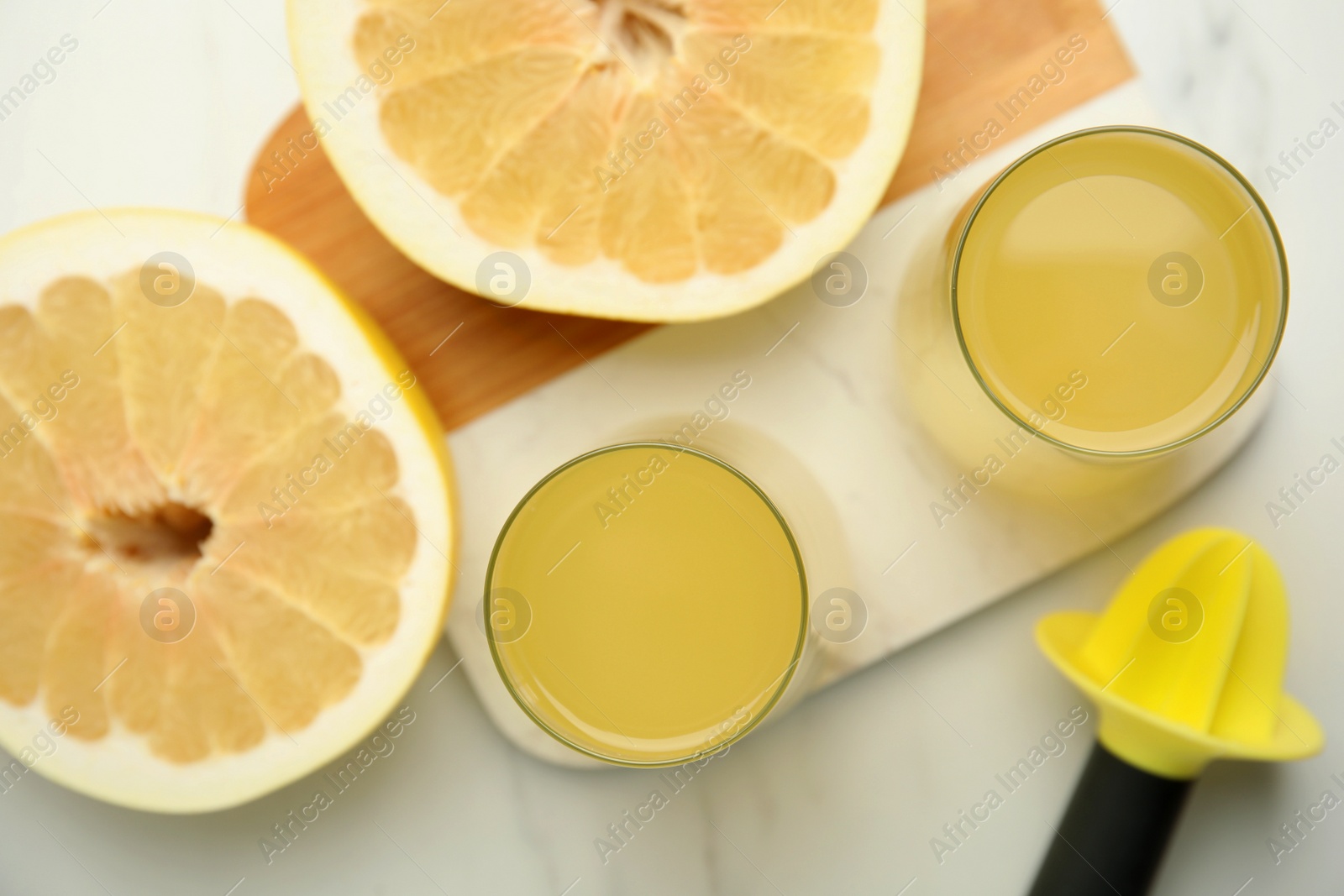 Photo of Glasses of fresh pomelo juice with reamer and fruit on white table, flat lay