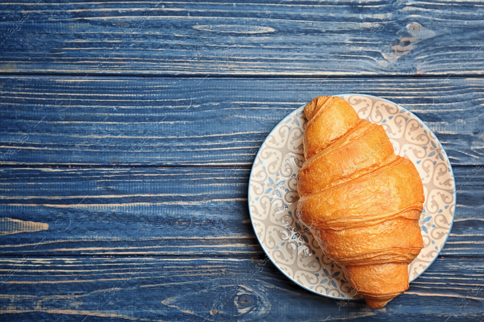 Photo of Plate with tasty croissant on wooden background, top view