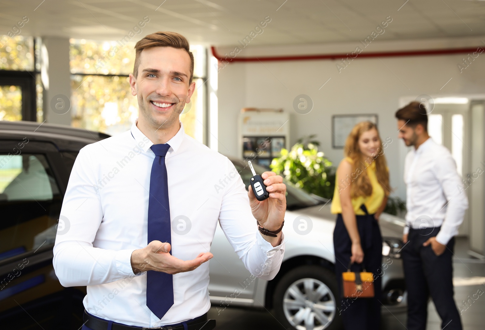 Photo of Young salesman with car key in dealership