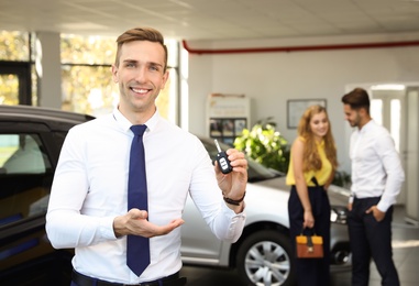 Young salesman with car key in dealership