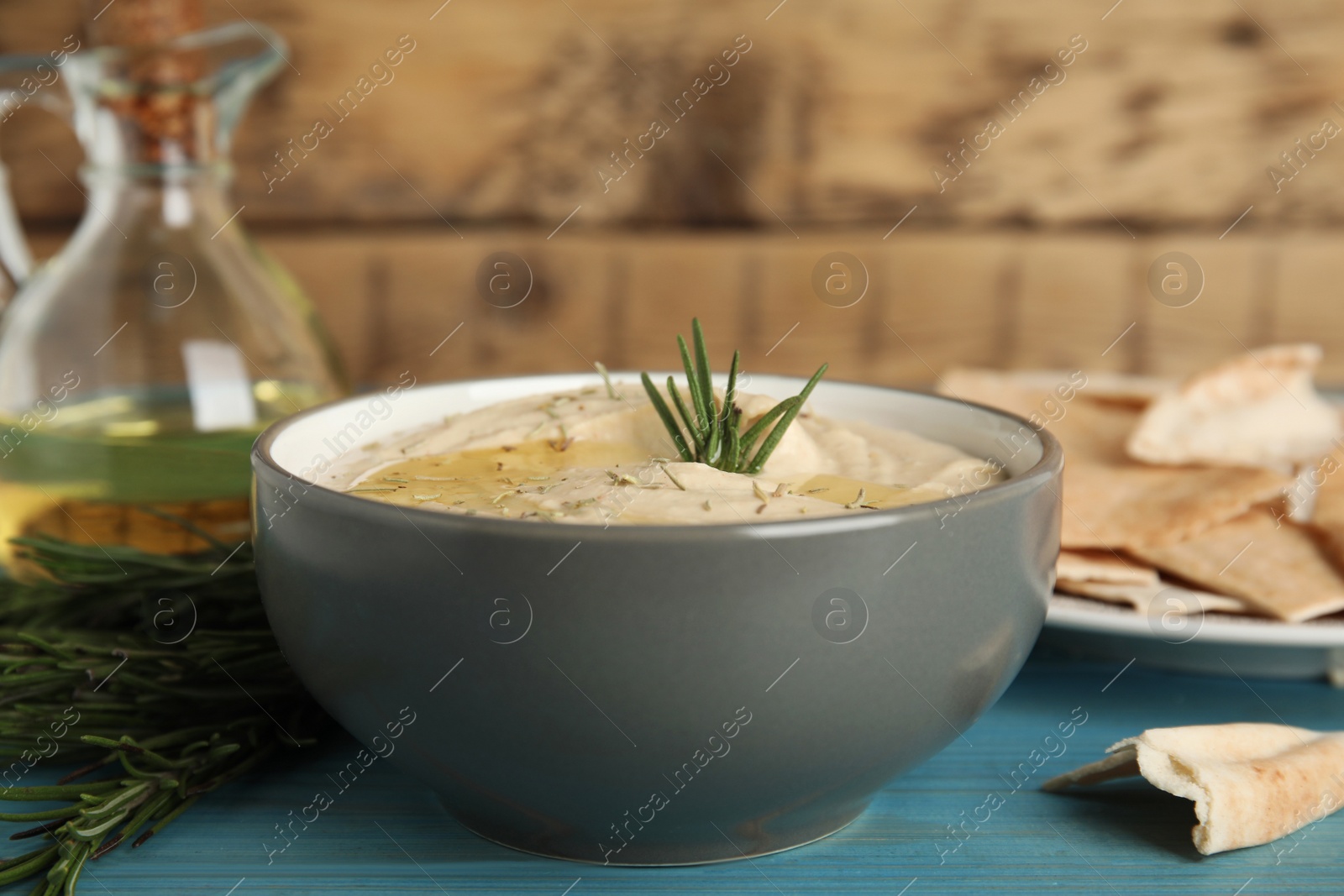 Photo of Delicious hummus with rosemary and pita chips on turquoise wooden table, closeup