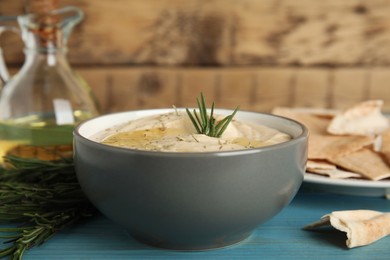 Delicious hummus with rosemary and pita chips on turquoise wooden table, closeup