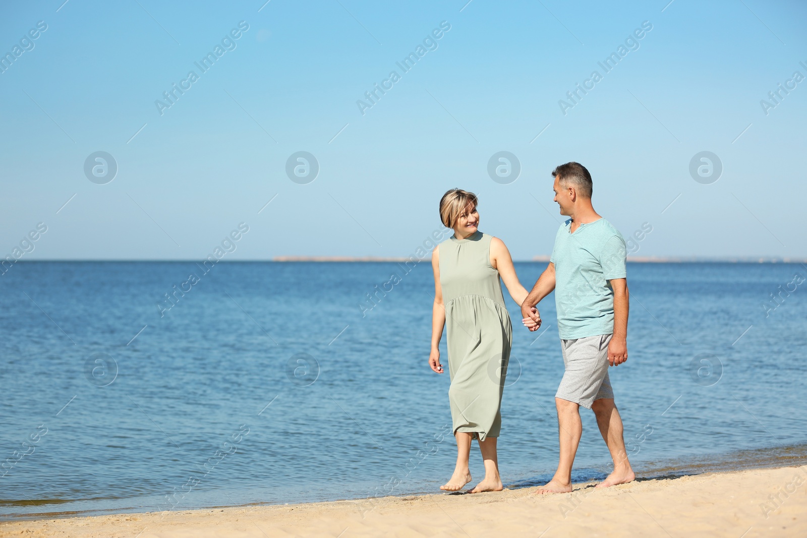 Photo of Happy mature couple holding hands at beach on sunny day