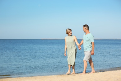 Photo of Happy mature couple holding hands at beach on sunny day